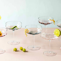 Set of Aida cocktail glasses with garnishes on a light pink surface