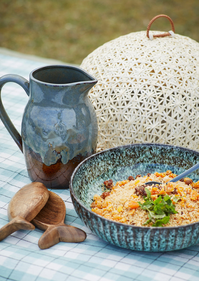 petrol blue and brown stoneware jug on a picnic table with rustic tableware
