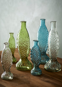 collection of coloured fish glass vases styled together on wooden surface
