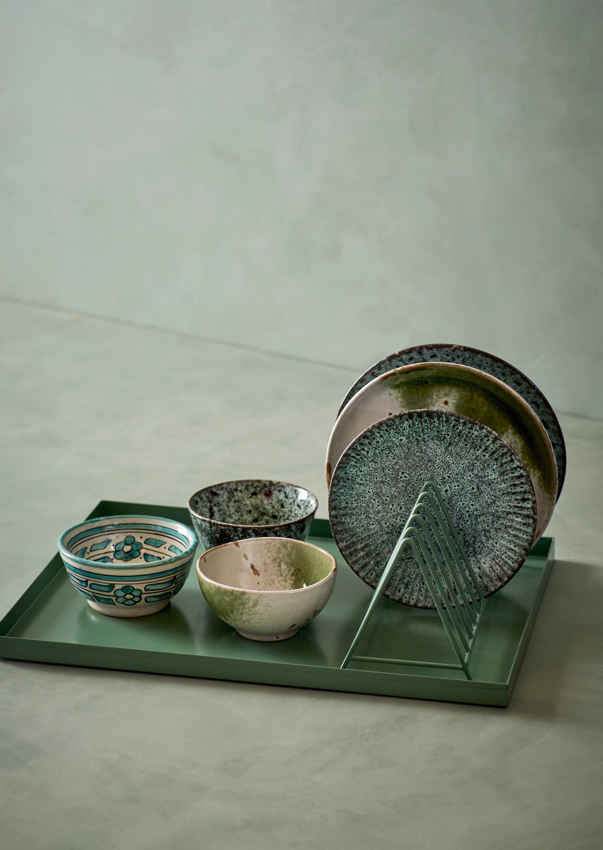 Set of ceramic bowls and plates on a green tray with a neutral background