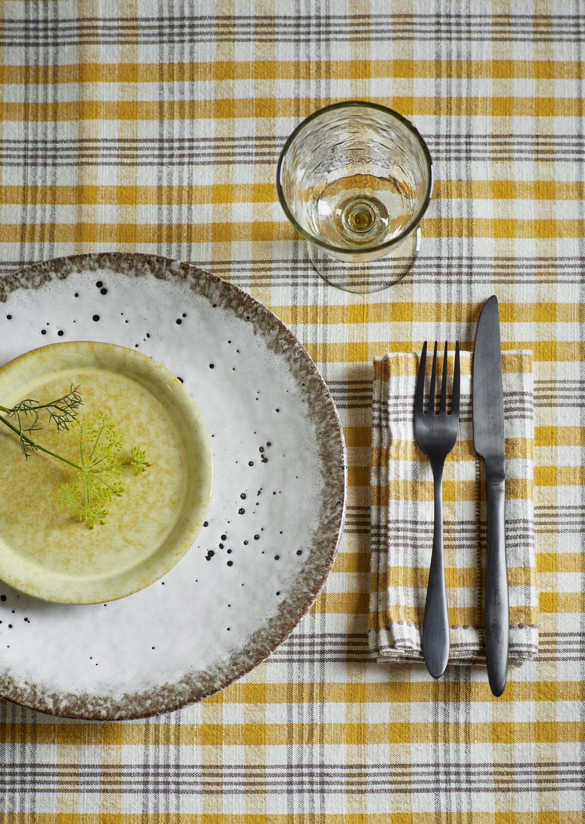 Dinner setting with a plate, glass, fork, and knife on a yellow and white checkered tablecloth.