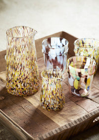 hand blown coloured drinking glasses and matching glass jug on a wooden table
