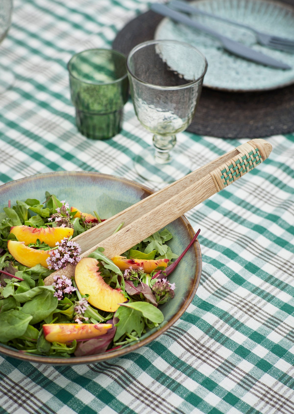 wooden tongs with green woven handle serving salad at outdoor table
