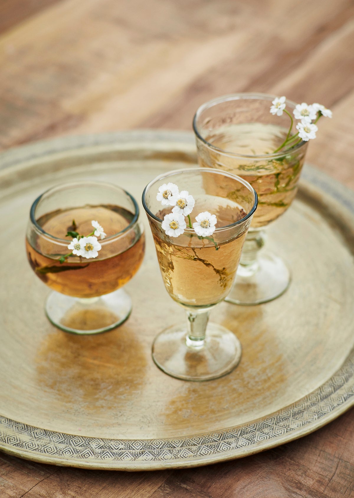 Three glasses of a beverage with white flowers on a decorative tray.