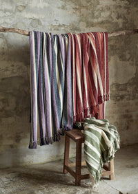 collection of recycled cotton throws in multiple colours hanging with green variant draped on stool
