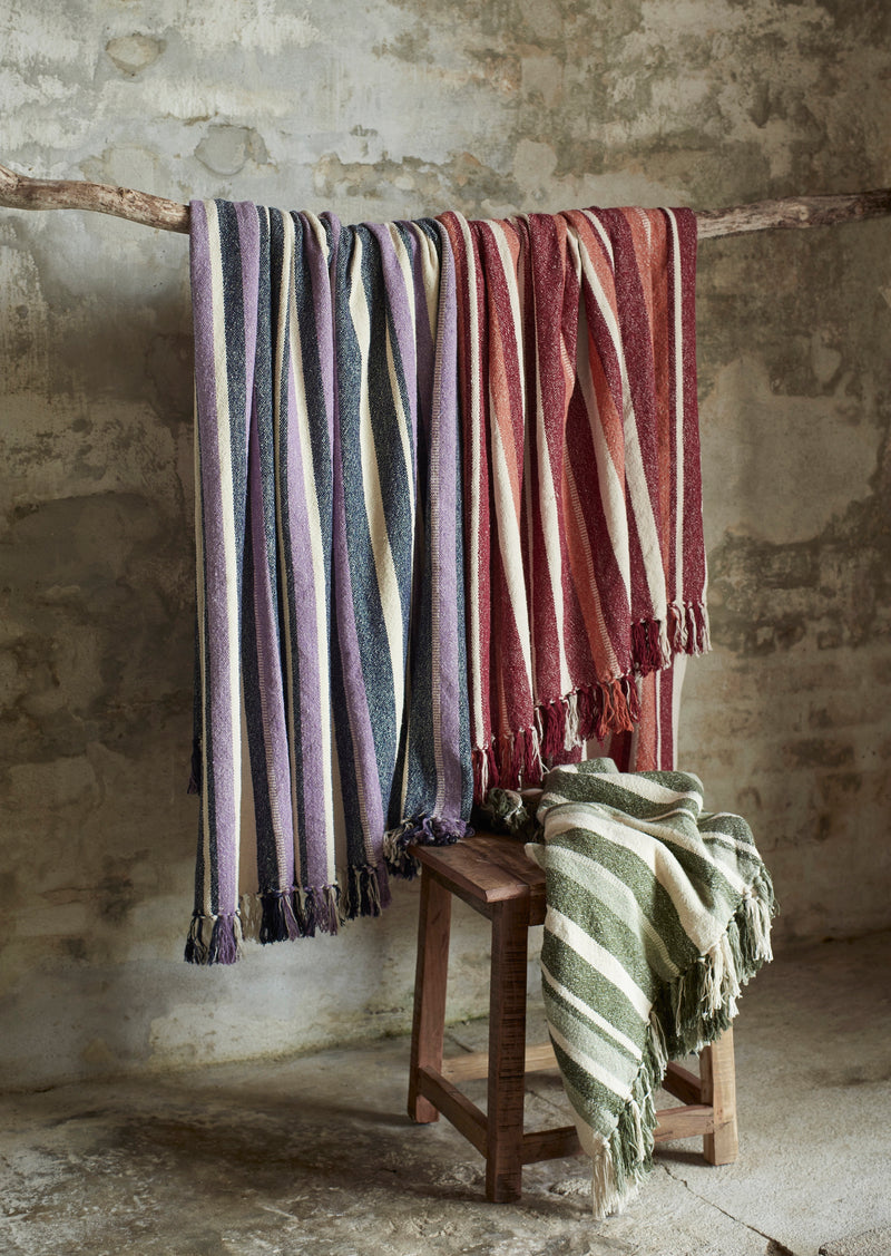 collection of recycled cotton throws in multiple colours hanging with green variant draped on stool
