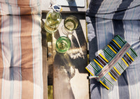Striped fabric pouch on a wooden table with glasses and a bottle.