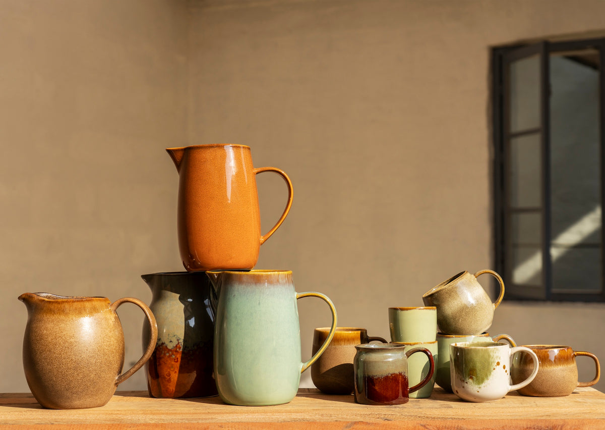 Collection of ceramic pitchers and mugs on a wooden surface with a neutral background