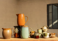 Collection of ceramic pitchers and mugs on a wooden surface with a neutral background