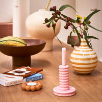 Talon tealight holder styled on a table with books, a striped vase and a pink candlestick