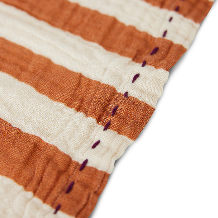 close up of an edge of a cloth napkin with tangerine and off white or beige stipe and purple stitching around the outer edge by nordic design house hk living