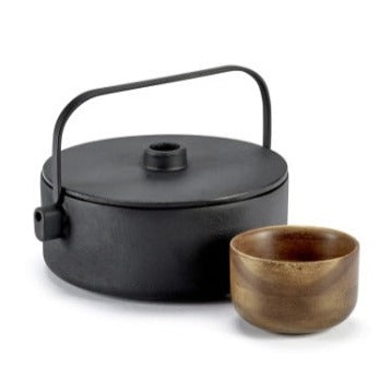 serax black cast iron tea pot that is an unusual shape in that although circular, it is flat on top although with a small handle to the lid and large, flattened handle going over the top to support pouring. he spout is unusal in that it is almost just a hole in the side of the pot