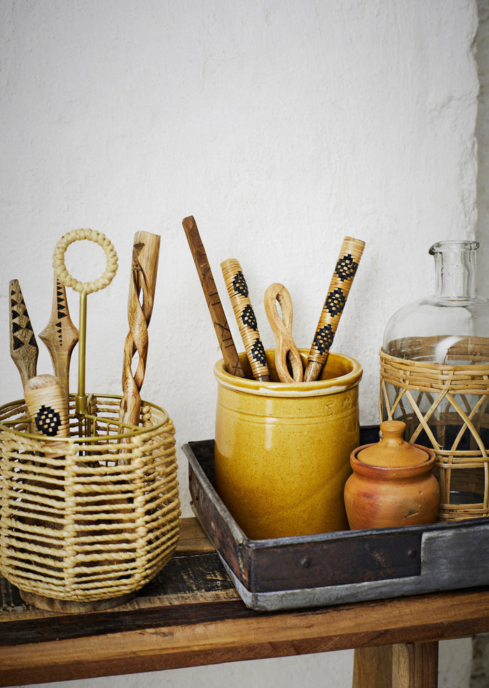 hand-carved wooden kitchen utensils with decorative handles in a rustic container