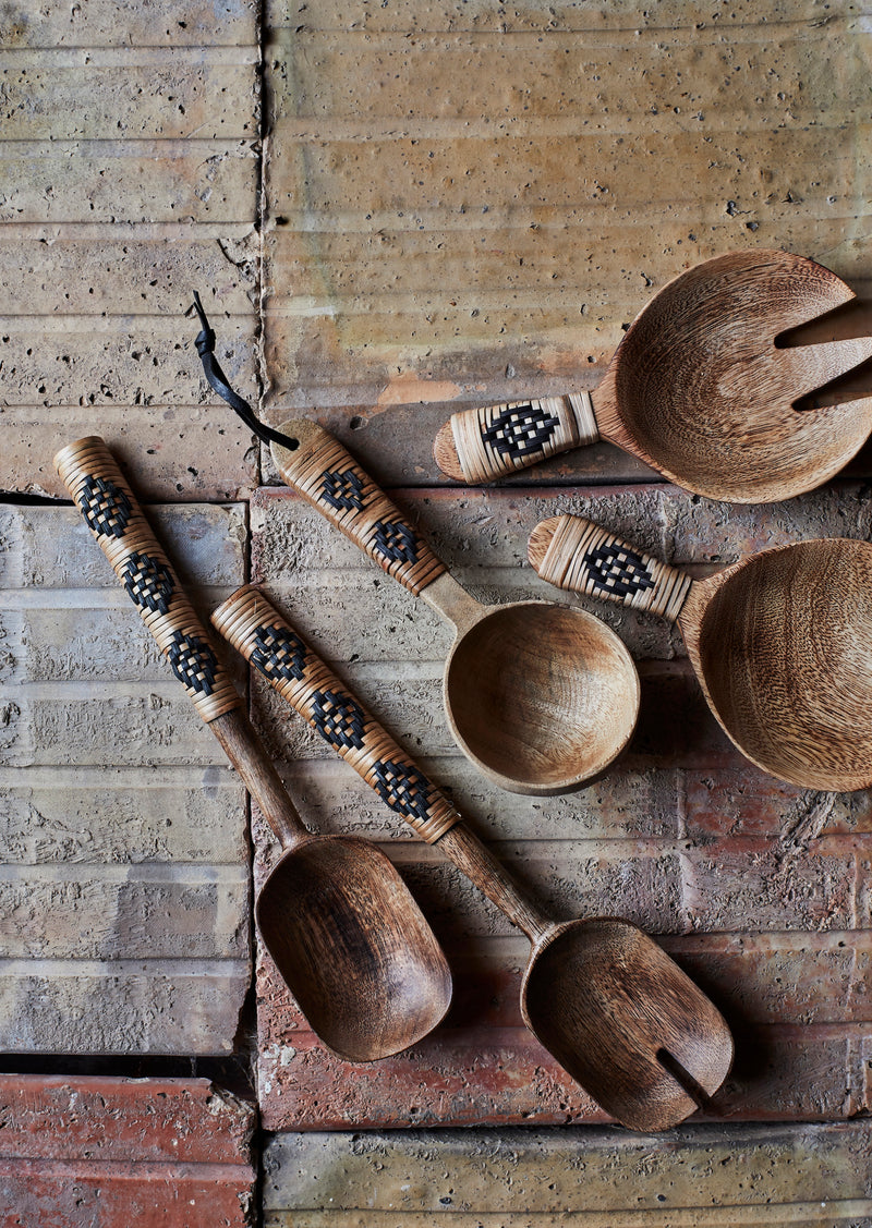 assortment of hand-carved wooden spoons with woven handles styled on rustic brick surface