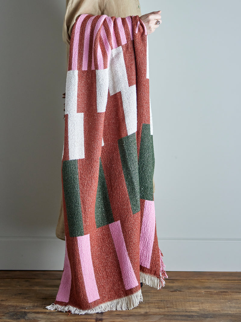 person holding recycled cotton york throw showing geometric pattern in red pink and green