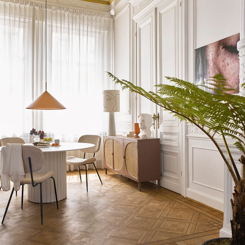 a dining room set-up with hklivnig lamps and objects on a side board and orange ceiling lamp hanginnig low above the dining table