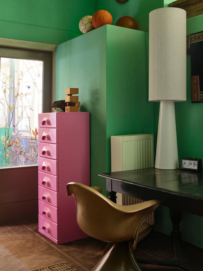 cream hkliving floor lamp stood on a dark wooden table with a pink hkliving chest of drawers all in a 70s green bedroom