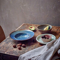 table set-up with avocado cut in half and whole walnuts in their shells alongside the blue of of a pasta plate from hkliving seated on a well worn wooden table